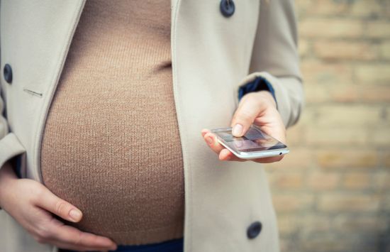 A photo of a pregnant woman's stomach as she looks at her cell phone