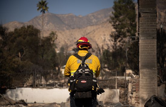 A firefighter stands among the remains of a building destroyed by a fire.