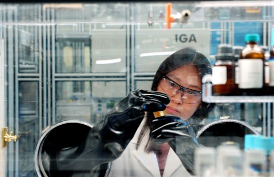 A researcher in a lab coat manipulates samples in an enclosed glove box.