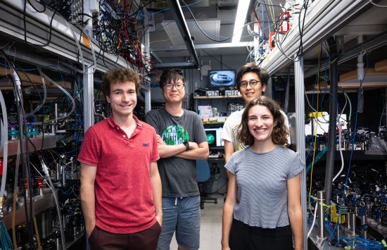 Four people (three men and a woman) stand inside a room with machines with lots of wires.