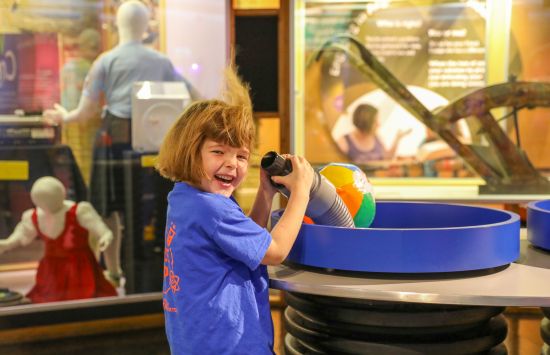 A young girl in a museum laughs as air blowing from a tube whips up her hair.