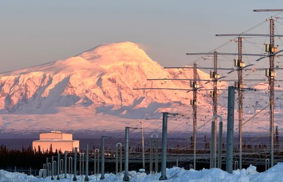 A snowy mountain in the distance with power lines and a square white building in the foreground.