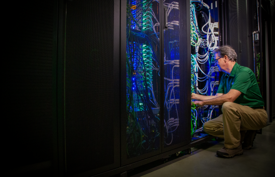 system administrator kneels to adjust the wires of a server rack