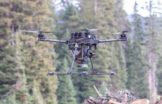 A drone hovers in mid-air in a forest.