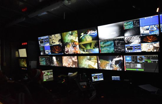 A wall of screens showing bright underwater images in a dark room.