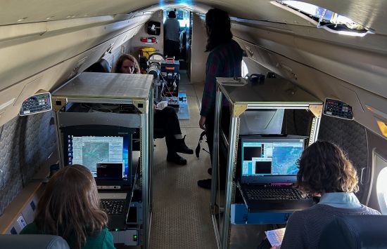 Researchers sitting at computer consoles inside an airplane during a solar eclipse.