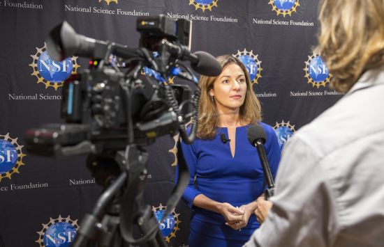 A woman speaks into a microphone in front of cameras at a press conference.