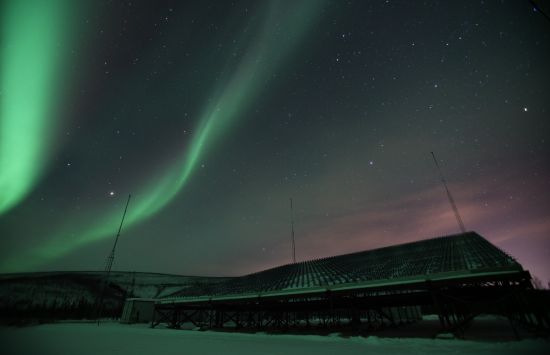 Green and purple northern lights over a low building.