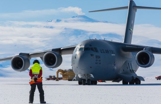 A C-17 cargo plane taxies across the frozen runway at the newly completed Phoenix airfield as a member of the ground crew guides the plane into place.