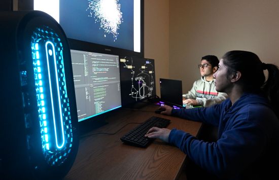 Two students work on computers while looking at a brightly lit screen.