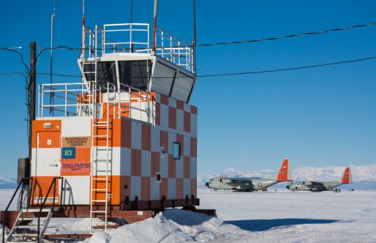Two LC-130 cargo planes sit parked on the frozen runway at Williams Airfield with the airport's control tower in the foreground.