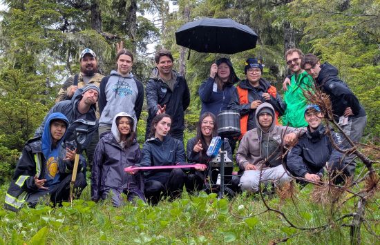 A group of smiling students in a rainy forest.