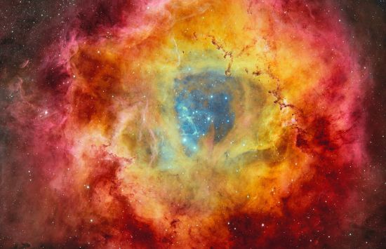 Stars on a dark blue background surrounded by clouds of a yellow, red and magenta nebula.