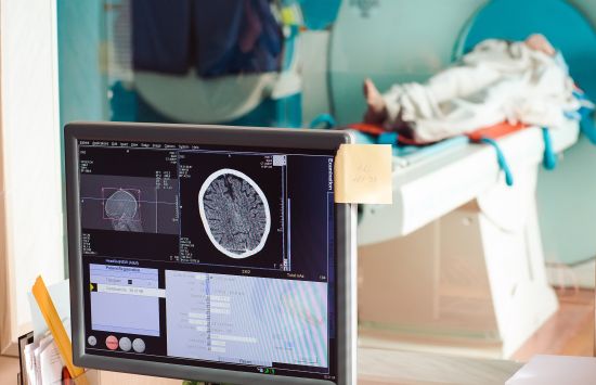 Stock photo an MRI machine with patient and screen in the foreground.
