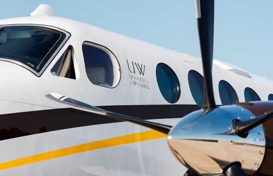 View of the cockpit window and one propeller of a plane with the University of Wyoming logo on the side.