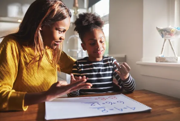 A woman and a child sit at a table with worksheets in front of them