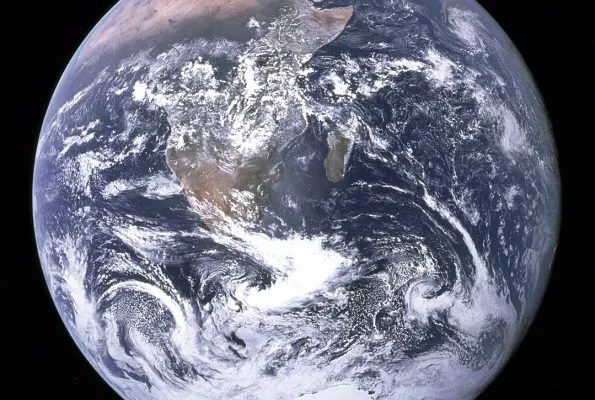 Photograph of the Earth with blue ocean and swirling white clouds set against the blackness of space