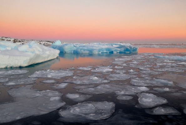 Ice floats on top of a body of water in front of a pink sky
