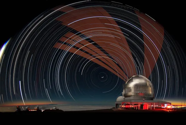 White and brown streams of light are seen in front of a night sky. To the right is a white domed building.