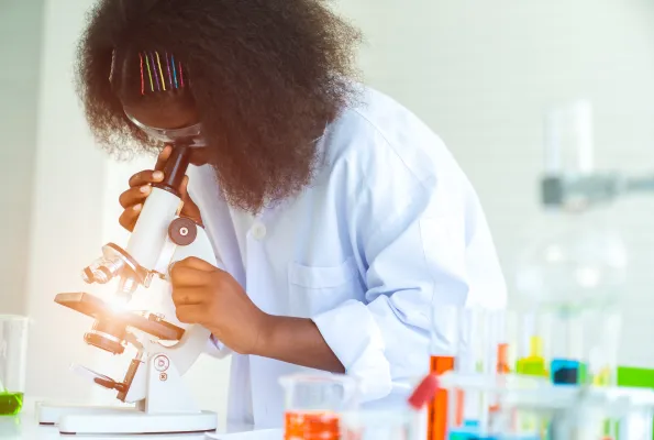 A young girl in a lab coat looks through a microscope