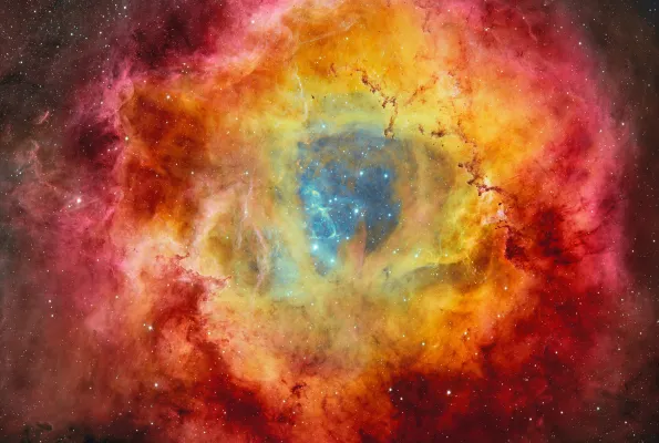 Stars on a dark blue background surrounded by clouds of a yellow, red and magenta nebula.