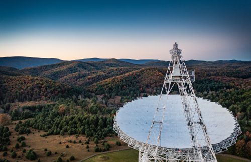 A radio telescope with rolling, tree-covered hills in the background