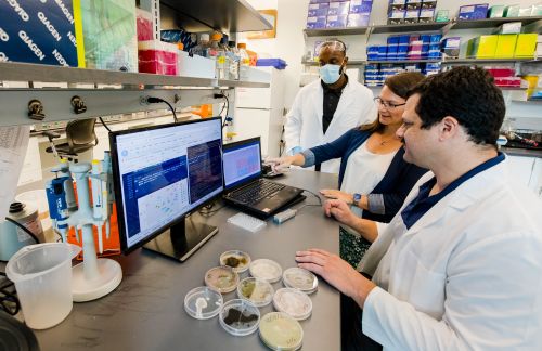 A group of researchers in a lab standing around a laptop that is displaying data