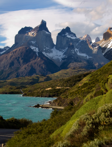 cyan lake at left below a snow-capped mountain background, bordered by green-covered hills to the right