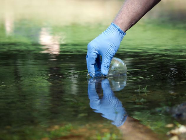 a gloved hand holding a bottle is submerged in a puddle of water