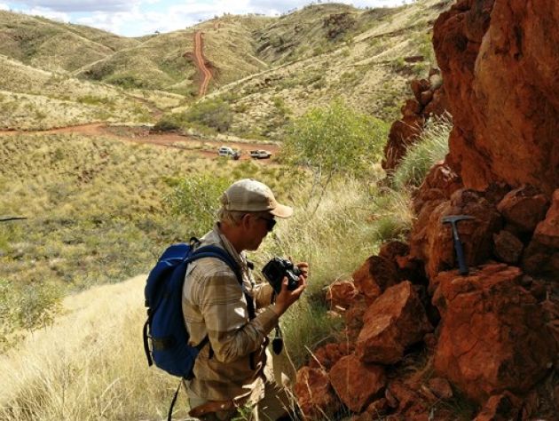 A man looks at a red rock outcropping with grassy rolling hills in the background