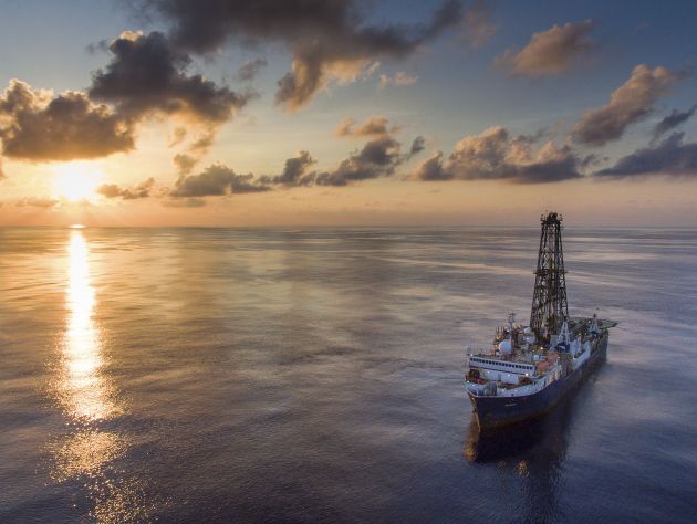 A large ship sails across a calm body of water with a sunset behind it