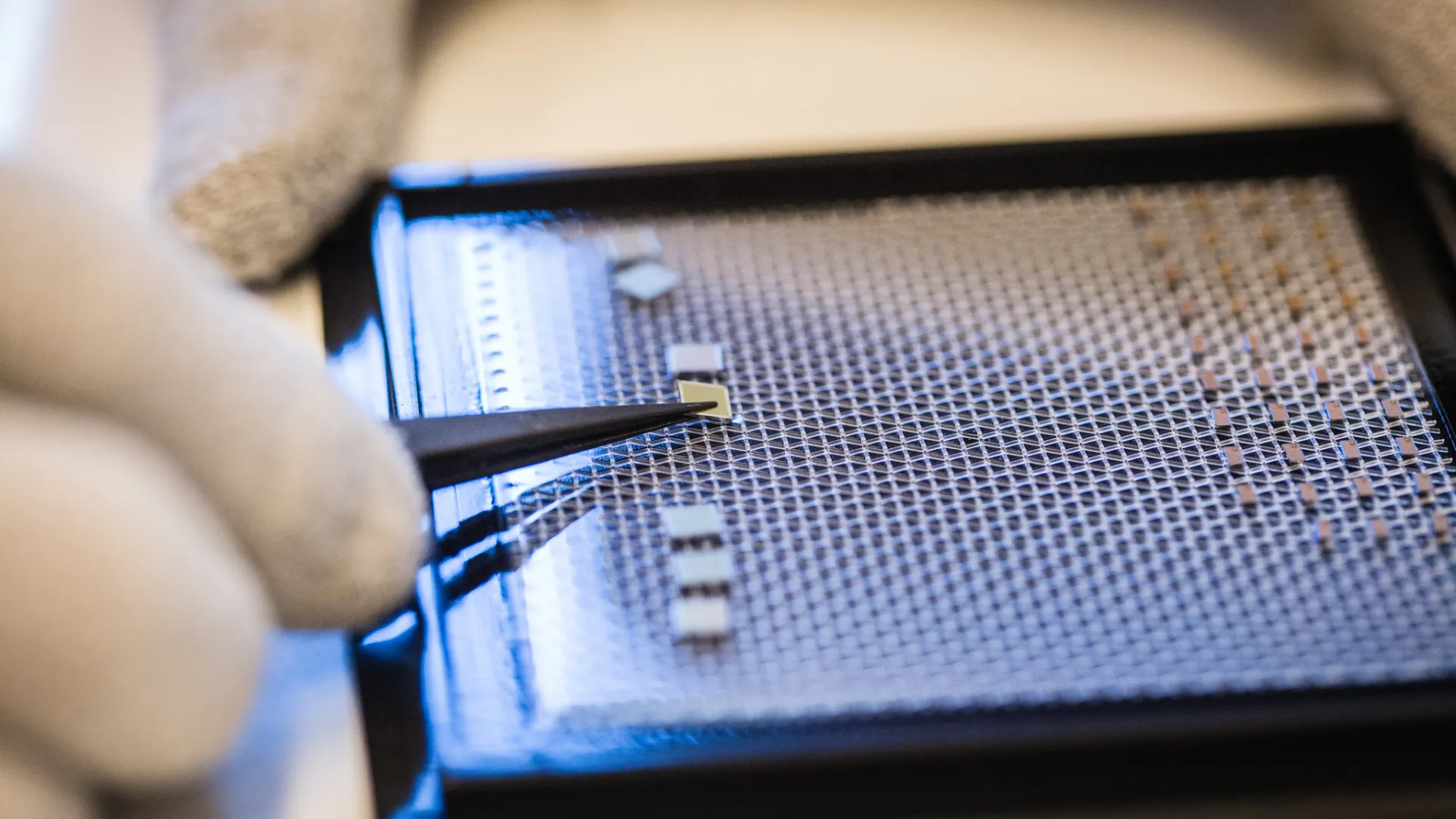 tweezers placing a computer chip on a screen.