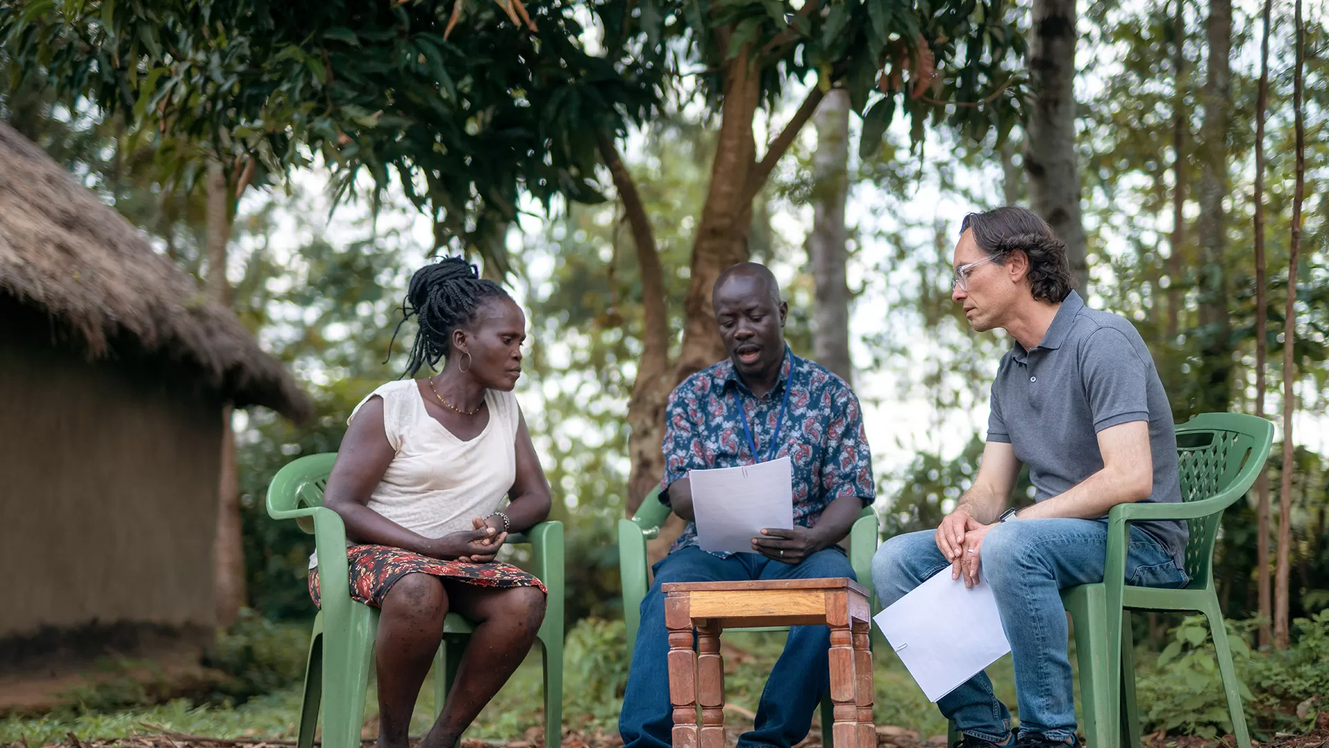 Researchers sitting in plastic chairs surrounded by trees outside a house in Kenya.