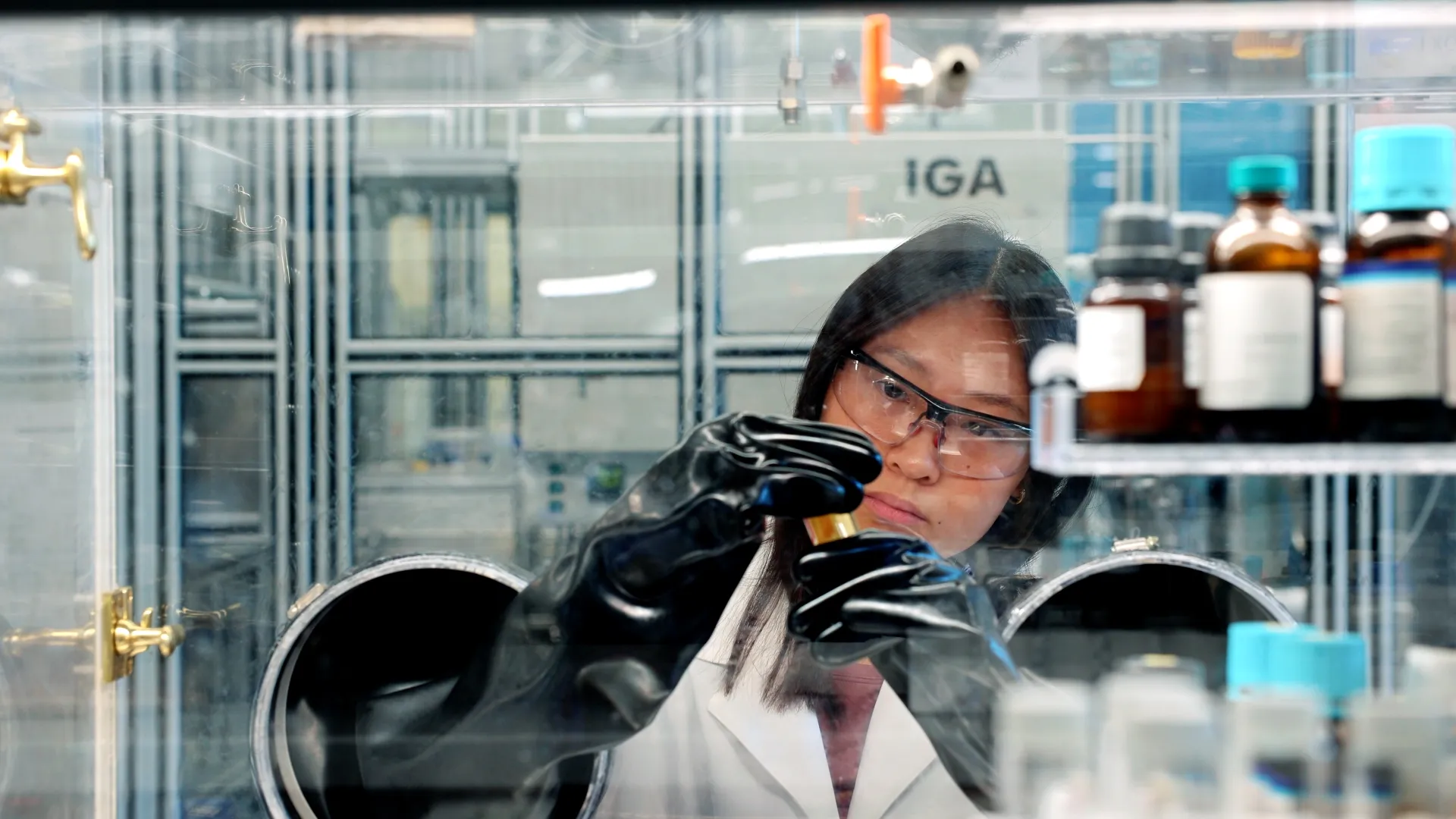 A researcher in a lab coat manipulates samples in an enclosed glove box.