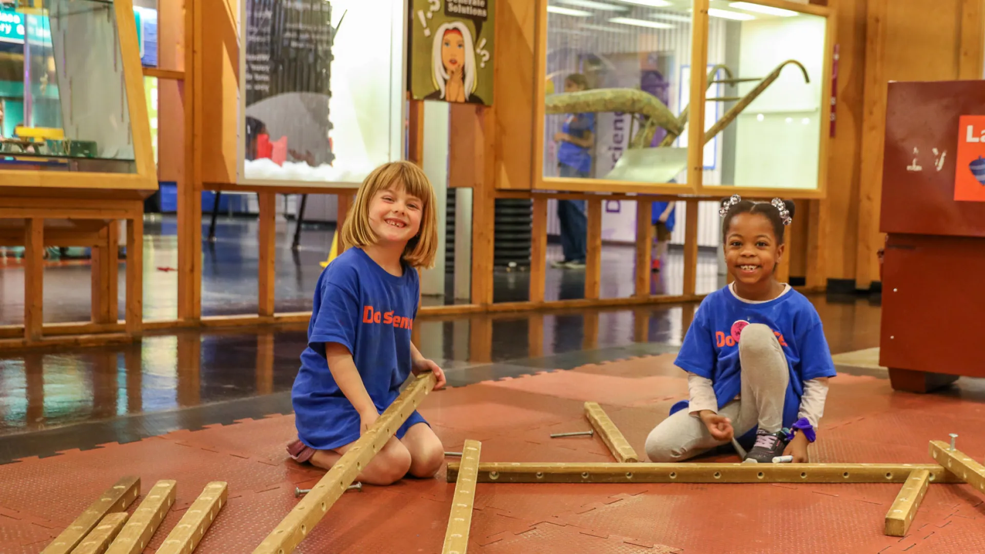 Two kids sitting on the floor in a science center building a wooden structure.