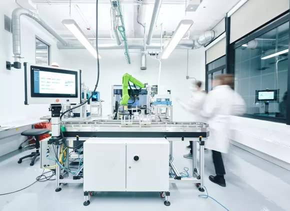 A blurred photo of lab workers moving around a bright laboratory