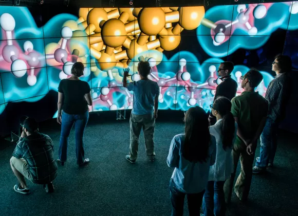 A researcher at the Electronic Visualization Laboratory discusses a visualization of a balls-and-sticks model of a molecular chemistry dataset on the CAVE2 System with students.