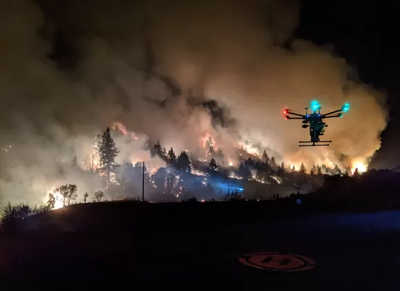 A drone hovers over its flight pad on the perimeter of a prescribed burn