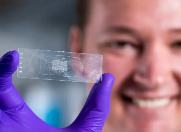 A graduate student displays a microscope slide holding an array of more than 300 microparticles