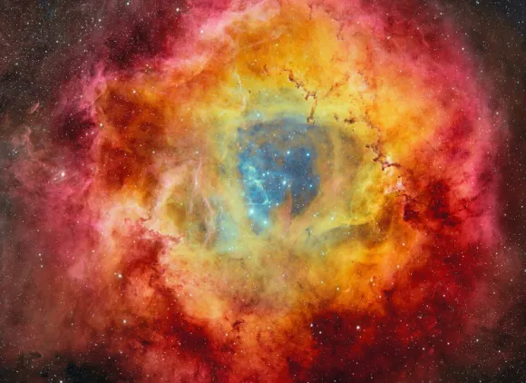 Stars on a dark blue background surrounded by clouds of a yellow, red and magenta nebula.