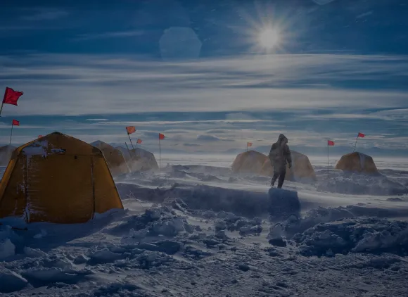 A person walks amidst yellow tents in a snowy, windy landscape.