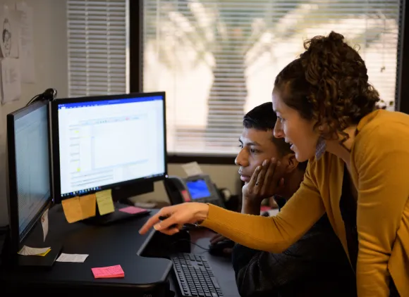 Two people looking at something on a computer with two monitors.