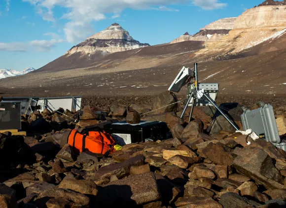 The photo shows a scientist adjusting equipment in Antarctica.