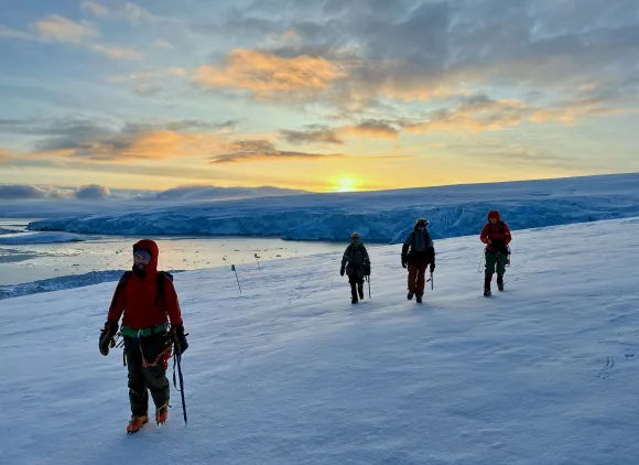 A satellite manager and members of the NSF Palmer Station Glacier Search and Rescue Team walk through the snow.