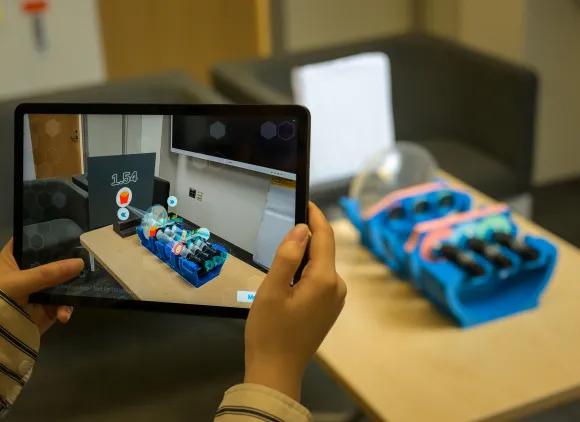 Hands holding a tablet displaying an augmented reality app.