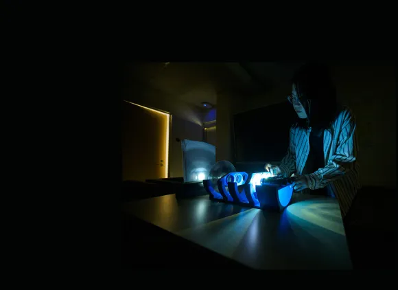 A research assistant in a dark room working on an illuminated device.