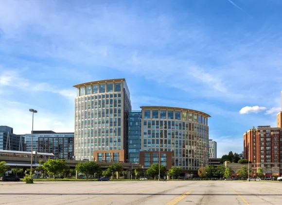 A Metro train sits parked at a station in front of a tall building.