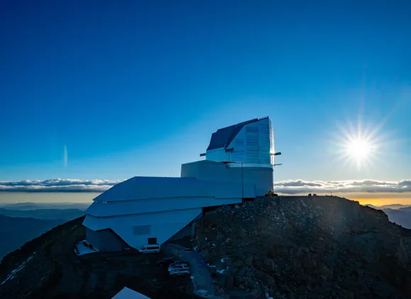 A building on top of a mountain with the sun in the distance.