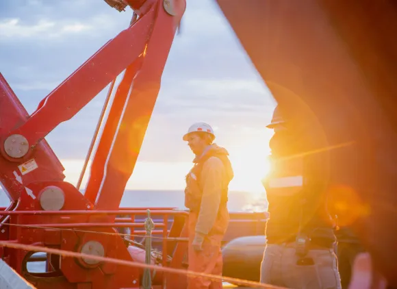 Researchers standing on a ship against a background of the glowing sun low on the horizon.