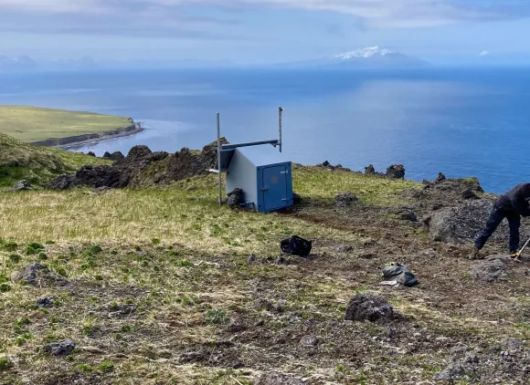 A technician installing a GPS station on a rocky cliff over the ocean.